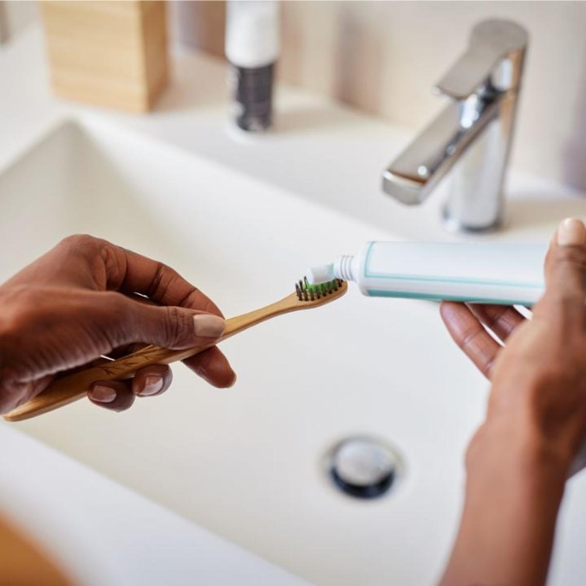 Toothpaste being put onto a toothbrush over a bathroom sink