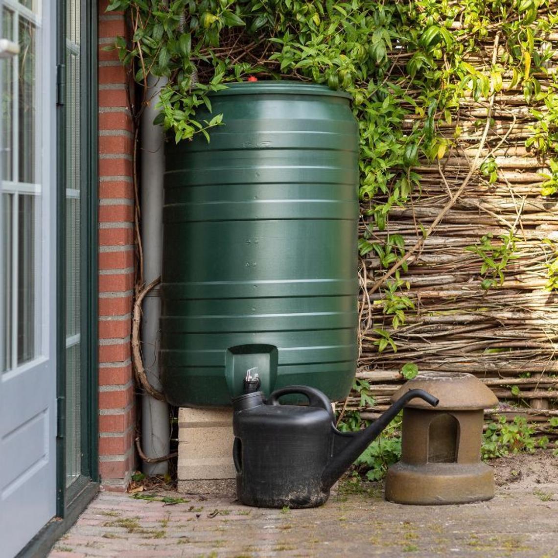Water butt next to a watering can outdoors on a garden patio