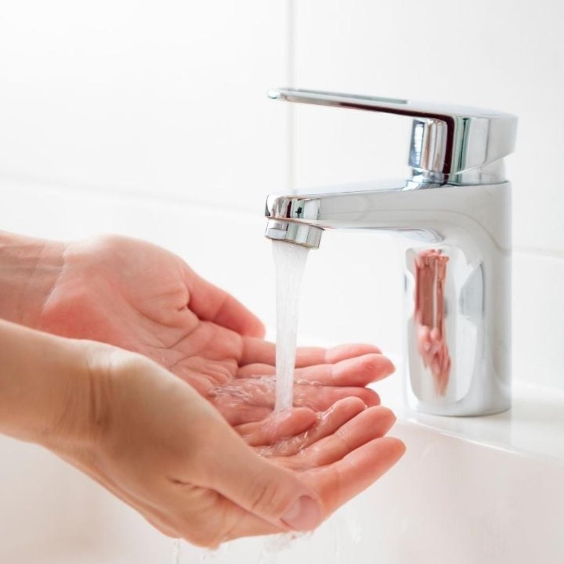 Water pouring onto persons hands from bathroom aerator tap