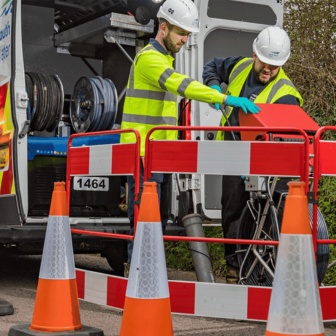 2 workers wearing hard hats and hi vis jackets by roadwork signs