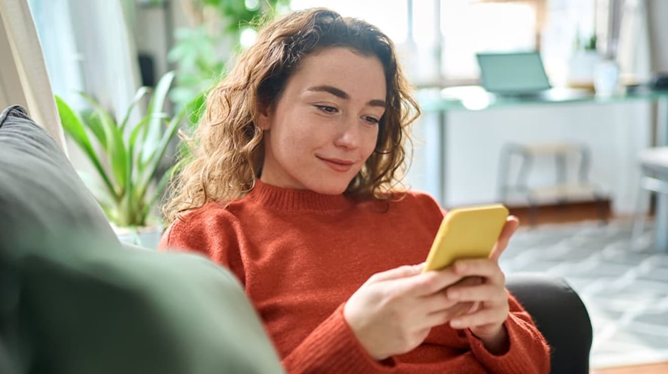 Image of a woman using her mobile phone whilst sat on the sofa